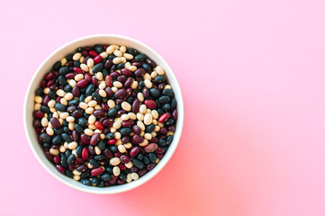 Mix of raw beans in a white bowl on a pink background. Top view and copy space.