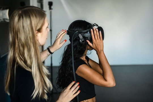 Caucasian young woman helps South-East asian girl putting on VR and controllers