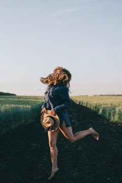 Emotional portrait of young female with long hair jumping and laughing in sunset light outdoors