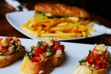 Dieses wundersch&ouml;ne essens bild zeigt im hintergrund ein sandwich mit french fries und im vordergrung eine leckere bruschetta mit saftig roten tomaten
