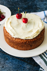 Homemade sour cream cake with cream cheese frosting decorated with fresh ripe cherries.