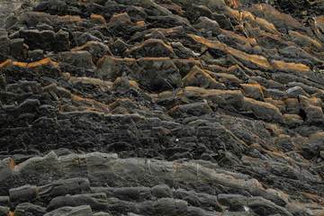 Dark natural black volcanic rock in layers as abstract texture background.
