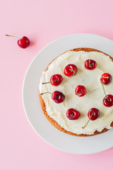Homemade sour cream cake with cream cheese frosting decorated with fresh ripe cherries on a light pink background. Top view.