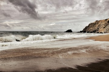 Brave ocean, rock formations and cloudy drama sky on the beach