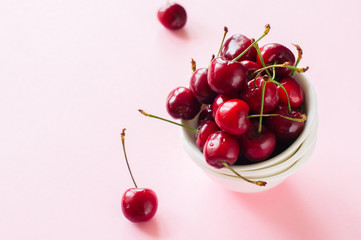 Obraz na płótnie Canvas Heap of fresh ripe red cherries in a white bowl on a pink background. Top view and copy space. Organic food concept.