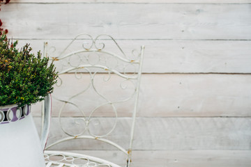 Details of garden with white vase and metal chair and table photographed against a simple wooden background with shallow depth of field. Concept for spring, summer garden, decoration and gardening.