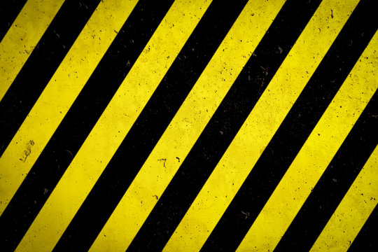 Warning sign yellow and black stripes painted over concrete wall coarse facade with holes and imperfections as texture background empty space. Concept for do not enter the area, caution, danger.
