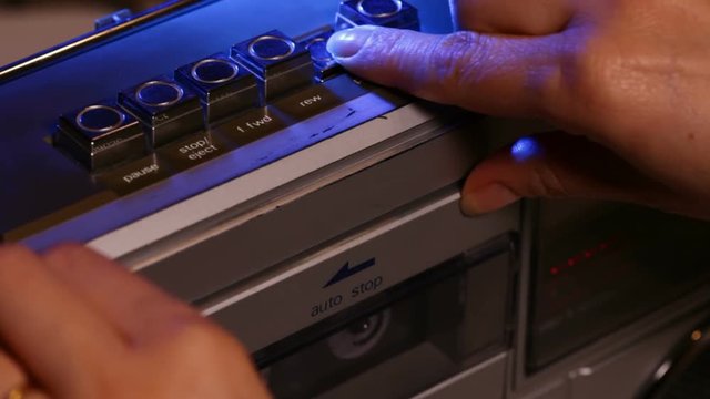 Woman hands place a compact music cassette tape in old retro player - closeup