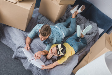 high angle view of happy young couple with album relaxing in bed after moving into new home