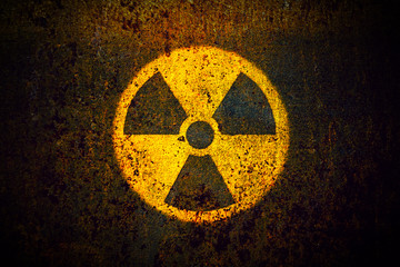 Round yellow radioactive (ionizing radiation) danger symbol painted on a massive rusty metal wall with dark rustic grungy texture background with vignetting. - 208054604