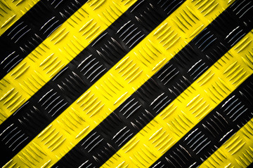 Warning sign yellow and black stripes painted over steel checker plate (or diamond plate) on the floor as texture background. Concept for do not enter the area, caution, danger, hazard.