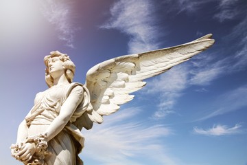 White angel marble sculpture with open long wings across the frame and against a bright sunny blue...