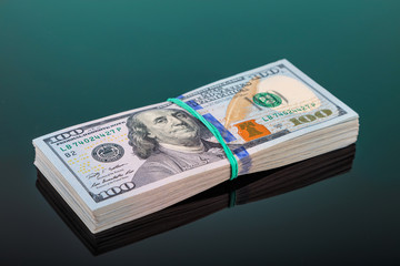 pack of 100 $ banknotes tied with an elastic band lies on a dark mirror surface
