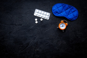 Medicine helps get asleep. Good sleep. Sleeping pills near sleeping mask and alarm clock on black background top view copy space