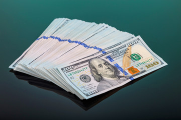 pack of 100 $ banknotes tied with an elastic band lies on a dark mirror surface