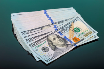 pack of 100 $ banknotes tied with an elastic band lies on a dark mirror surface