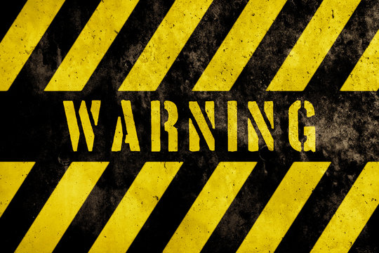 Warning sign text with yellow and dark stripes painted over concrete wall facade texture background. Concept image for caution, danger and hazard.