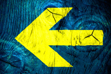 Yellow arrow direction sign over vivid bright blue color wooden wall with imperfections and cracks...