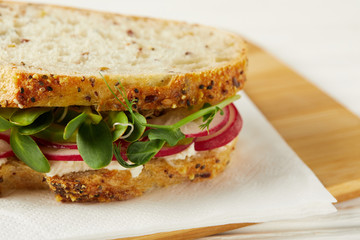 close-up shot of fresh sandwich with radish slices and pea shoots on wooden cutting board