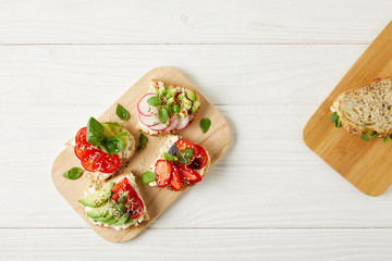 top view of various sandwiches on cutting board on white wooden surface