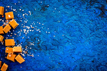 Fototapeta na wymiar Trendy dessert. Salted caramel. Caramel cubes sprinkled by salt crystals on blue background top view copy space