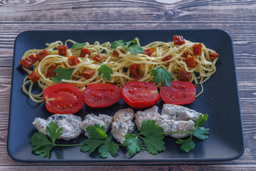 white meat and spaghetti with red tomatoes and parsley close-up