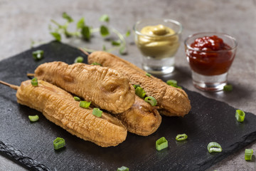 Four fresh corn dogs o a dark slate with tomato sauce and mustard