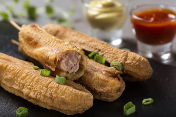 Four fresh corn dogs o a dark slate with tomato sauce and mustard