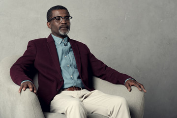 serious stylish african american man sitting in armchair