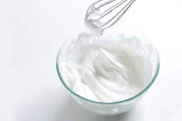 Whipped eggs in a bowl with a whisk on a white table