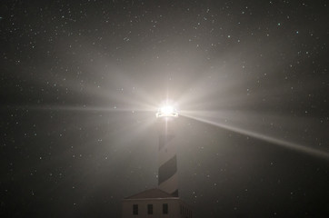 Landscape photograph of a Menorca lighthouse at night giving light and stars in the background.