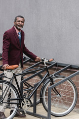 fashionable mature african american businessman with bike on parking for bicycles