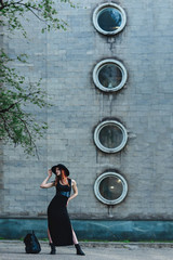 Fototapeta na wymiar Creative redhead woman in gothic black dress and hat in the city. Street style