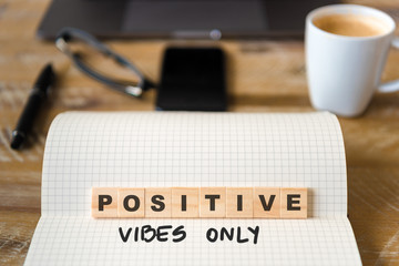 Closeup on notebook over wood table background, focus on wooden blocks with letters making Positive Vibes Only text