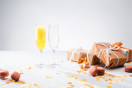 Close Up View Of Glassware With Yellow Champagne, Macarons And Arranged Gifts On Grey Backdrop