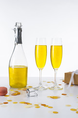 close up view of bottle and glasses with yellow champagne and wrapped gift on grey backdrop