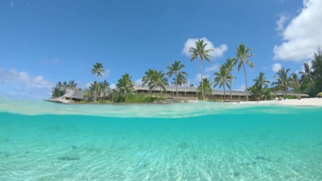 HALF UNDERWATER: Remote wooden resort surrounded by palm trees and stunning crystal clear ocean looking at the empty white sand beach in Cook Islands. Picturesque view of tropical oceanfront hotel.