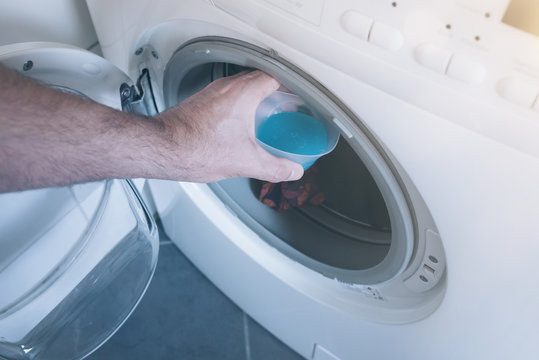male hand placing measuring cap with laundry detergent in washer