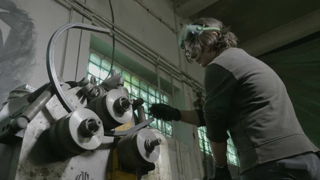 Woman blacksmith doing a bending test with an iron bar and a new bending machine in her workshop