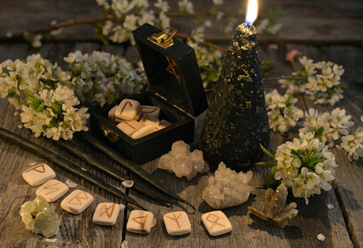 Black candles with old runes, crystals and flowers on planks. Occult, esoteric and divination still life. Halloween background with vintage objects 