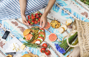 Picnic setting on the grass with basket, sandwiches, fruit, strawberry, salad and olives