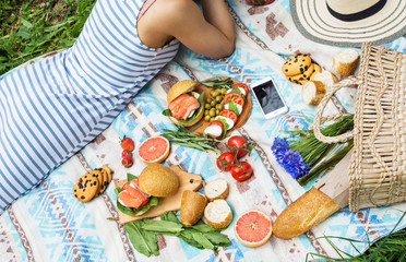 Picnic setting on the grass with basket, sandwiches, fruit, strawberry, salad and olives.