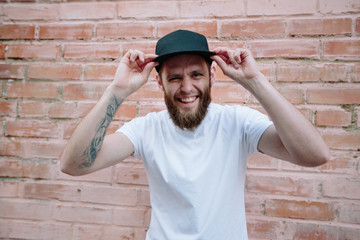 Hipster handsome male model with beard wearing white blank t-shirt and a baseball cap with space for your logo or design in casual urban style