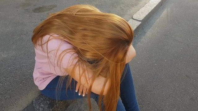 Frustrated girl sitting on sidewalk, victim of pickpocket crying in street