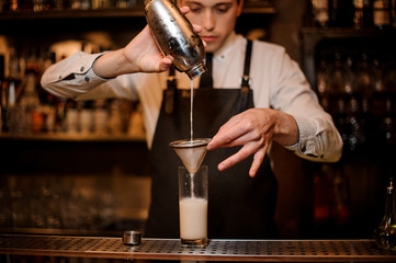 Bartender pouring an alcoholic drink from the steel shaker