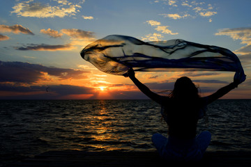 A young slender girl stands on a wooden bridge (fishing bridge) spreading her hands over the sea and looking at the sunset (dawn) of the sun. Life and freedom. 