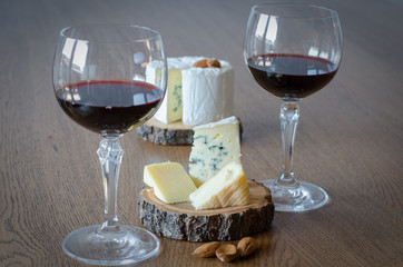 Two glass of red wine with few pieces of cheese at wooden background