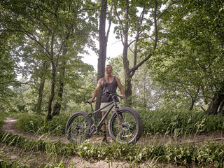 A trained man is riding a fat bike along forest paths.