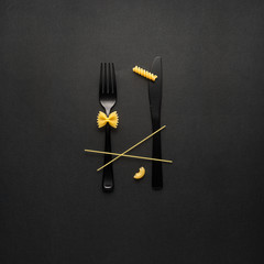 Tasty pasta / Creative still life photo of fork and spoon with raw pasta on black background.