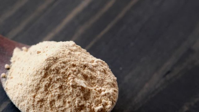 Superfood maca powder in wooden spoon rotating on wooden table top
